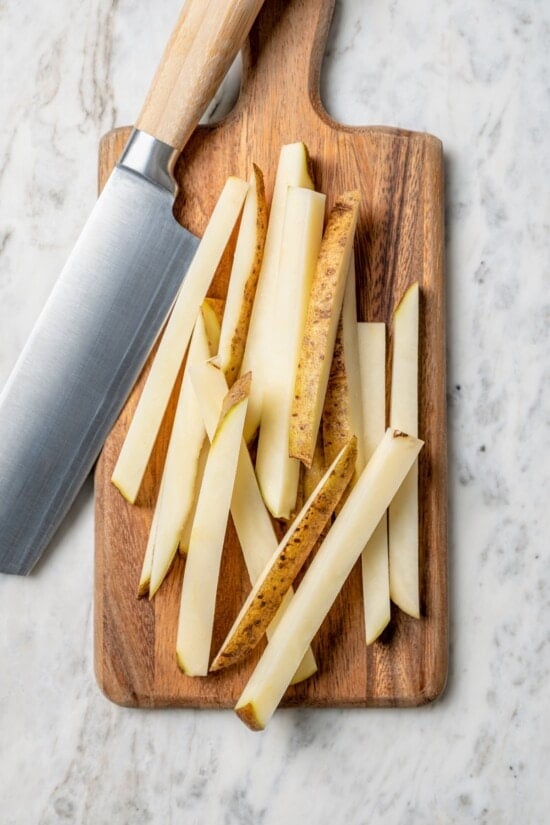 Overhead view of potato cut into fries on cutting board